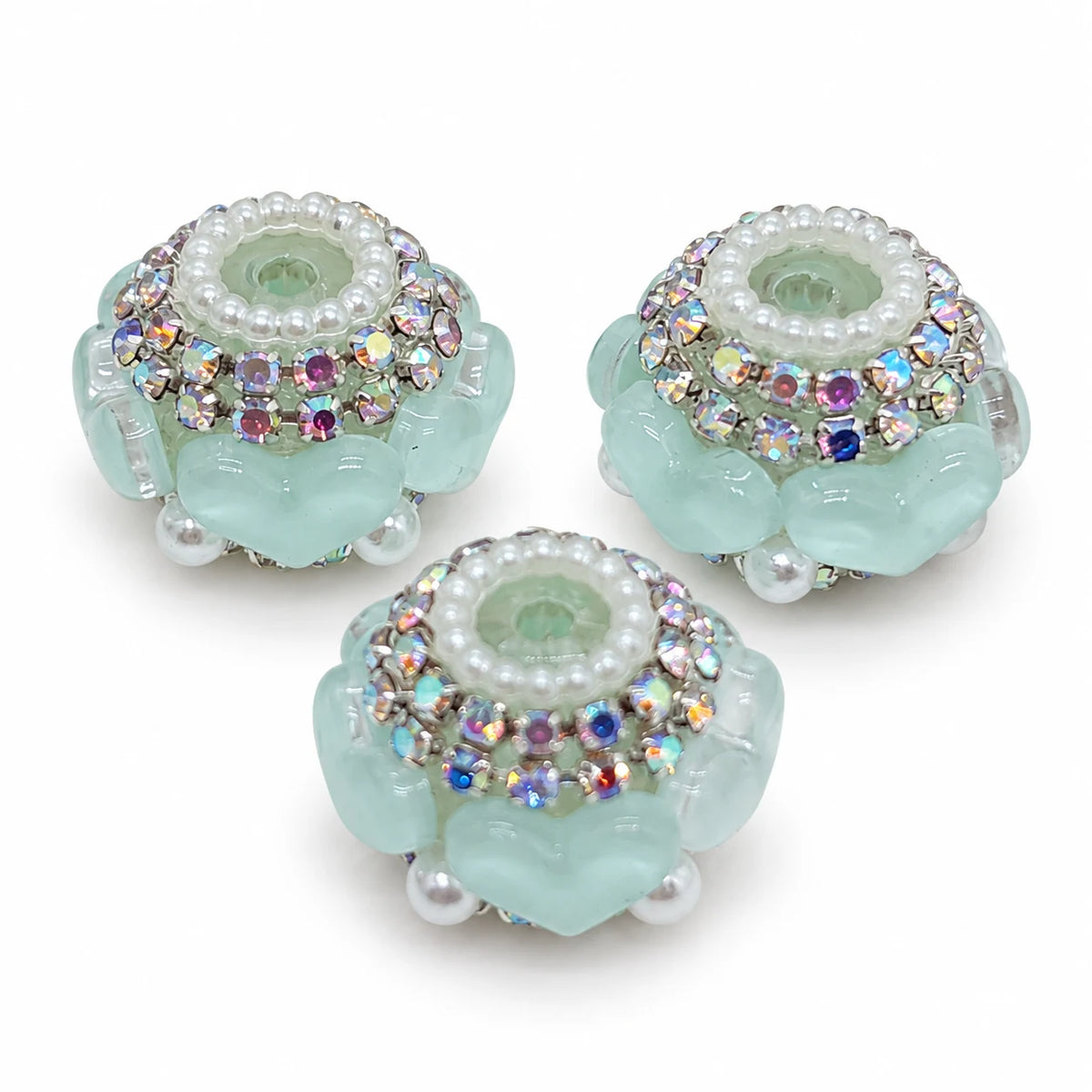 Three aqua acrylic heart barrel beads with silver-tone rhinestone trim and pearl-like accents on a white background
