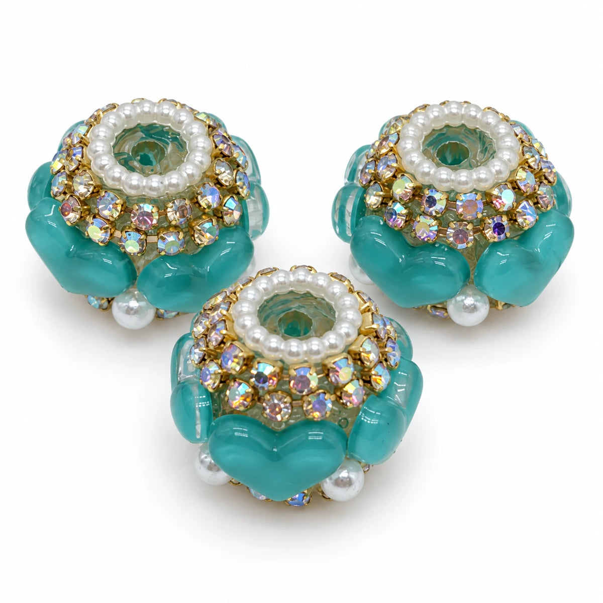 Three teal green acrylic heart barrel beads with gold-tone rhinestone trim and pearl-like accents on a white background