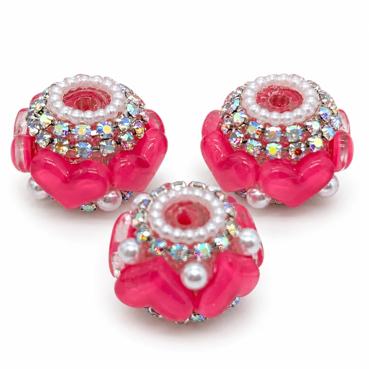 Three hot pink acrylic heart barrel beads with silver-tone rhinestone trim and pearl-like accents on a white background