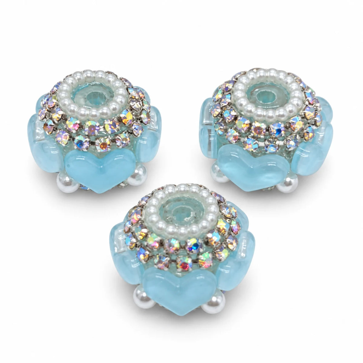 Three light blue acrylic heart barrel beads with silver-tone rhinestone trim and pearl-like accents on a white background