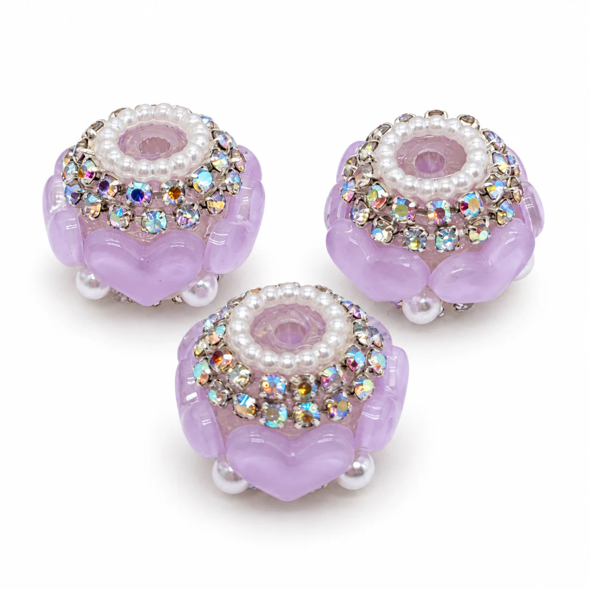 Three light purple acrylic heart barrel beads with silver-tone rhinestone trim and pearl-like accents on a white background