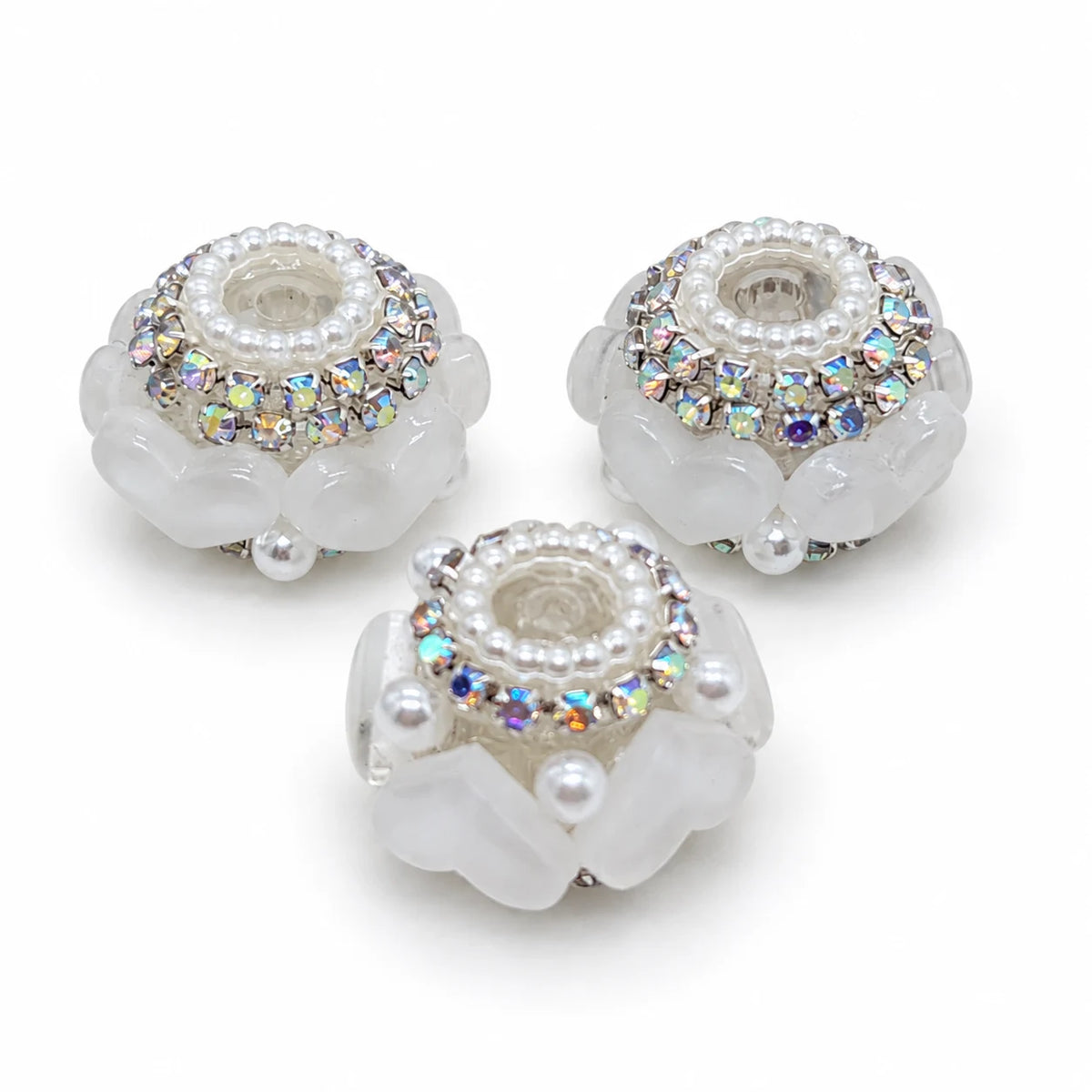 Three white acrylic heart barrel beads with silver-tone rhinestone trim and pearl-like accents on a white background